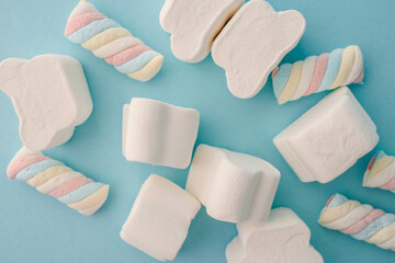 Fluffy white marshmallows in various shapes scattered on a light blue background. Minimalist and playful arrangement ideal for confectionery, dessert, or fun food themes