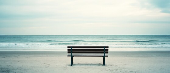 A solitary bench overlooks a calm beach, inviting peaceful reflection against a soft blend of sea and sky, evoking tranquility.