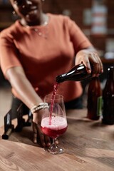 Vertical shot of female African American sommelier pouring craft cider into glass during product sampling in tasting room as part of factory, copy space