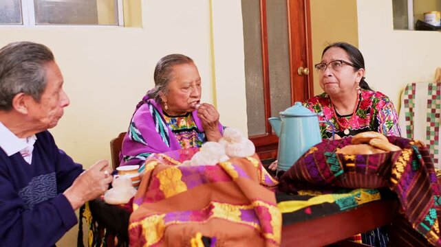 Two elderly Latino women and a man chat while sharing a cup of coffee and artisanal bread made with organic ingredients.