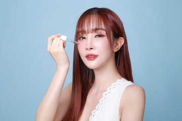 Obraz premium Beautiful young Asian woman model long hair using dropper bottle to apply serum on face clean fresh skin on isolated blue background. Cute girl portrait, Facial treatment, Body care, Beauty and Spa.