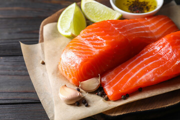 Pieces of fresh salmon, garlic, lime, oil and spices on wooden table, closeup