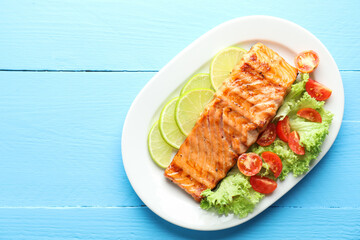 Delicious grilled salmon fillet with vegetable salad and lime on light blue wooden table, top view. Space for text