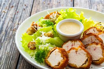 Caesar style salad - delicious grilled chicken breast slices and fresh vegetables and seasonings served on white plate on wooden table 
