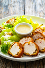 Caesar style salad - delicious grilled chicken breast slices and fresh vegetables and seasonings served on white plate on wooden table 