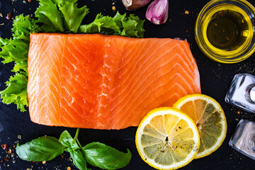 Fresh raw salmon steak with fresh vegetables on black stony board on wooden background
