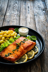 Seared salmon steak with gnocchi and lemon slices served on black plate on wooden table
