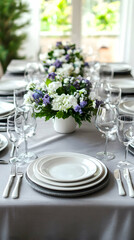 Fototapeta premium A beautifully set table with white plates, silverware, glasses, and a centerpiece of white and purple flowers.