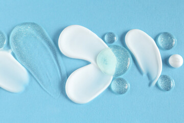 Smears of different cosmetic products on light blue background, top view