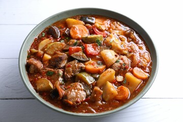 Delicious stew with vegetables in bowl on white wooden table, closeup