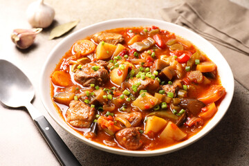 Delicious stew with vegetables in bowl and spoon on light grey table, closeup