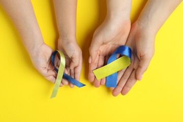 Woman with child holding yellow and blue ribbons on color background, top view. Down syndrome awareness