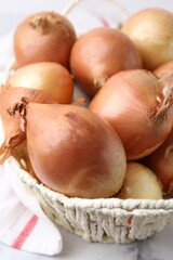 Fresh onions with peels in wicker basket on light table, closeup