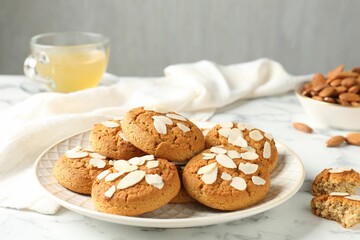 Tasty cookies with almond flakes, nuts and tea on white marble table, closeup