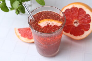 Glass of drink with chia seeds and grapefruit on white tiled table, closeup