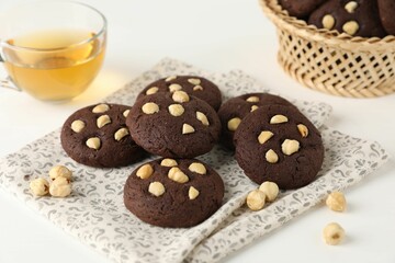 Tasty chocolate cookies with hazelnuts and tea on white table, closeup