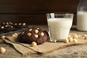 Tasty chocolate cookies with hazelnuts and milk on wooden table, closeup