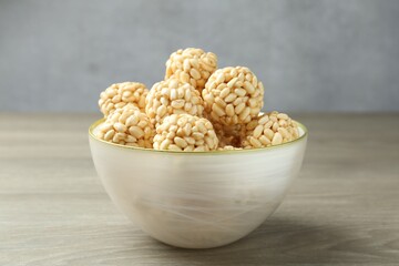 Tasty puffed rice balls in bowl on wooden table, closeup