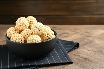Tasty puffed rice balls in bowl on wooden table, closeup. Space for text