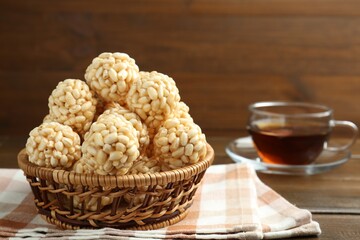 Tasty puffed rice balls in wicker basket and tea on wooden table, closeup