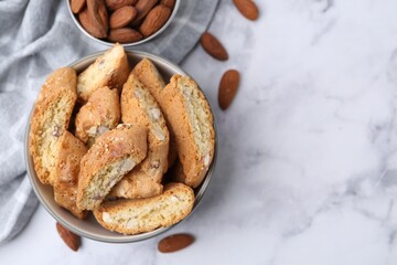 Tasty almond biscuits (Cantuccini) in bowl and nuts on light marble table, flat lay. Space for text