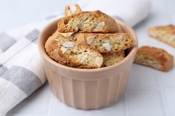Tasty almond biscuits (Cantuccini) in bowl on white tiled table, closeup