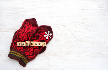 knitted red mittens, word "january" of wooden letters, decorative snowflake on white wooden background. january month calendar concept. winter season. top view