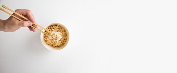 Female hand takes Chinese noodles with Chinese chopsticks from a paper bowl on a white background. Top view, fly lay. Banner