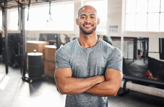 Portrait, fitness and happy man with arms crossed for exercise, body health or wellness in gym. Face, smile or confident African bodybuilder, personal trainer or strong athlete with muscle in Nigeria