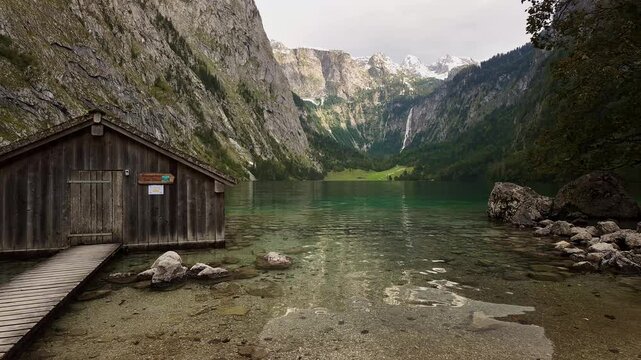 A cabin amidst the crystal clear lake of Obersee  with reflective water in the foreground at Berchtesgaden National Park Bavaria Germany Serene Landscape with waterfall Bavarian Alps in the backdrop