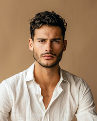 Fototapeta premium A man with curly hair and a beard poses in a white shirt against a brown background