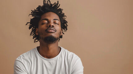 Fototapeta premium A young man with dreadlocks stands in front of a light brown background with his eyes closed