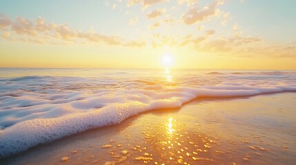 Obraz premium A serene beach at sunrise with gentle waves lapping against the shore, reflecting warm hues of orange and yellow in the water.