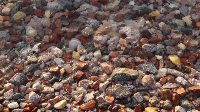 Background with transparent water of red sea calm surf covers red and white beach pebbles close up