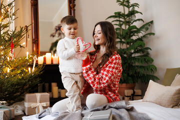 Parent and child holding candy canes in heart shape near presents and Christmas tree at home