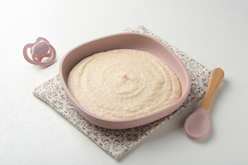 Delicious baby food in bowl with spoon and pacifier on white background