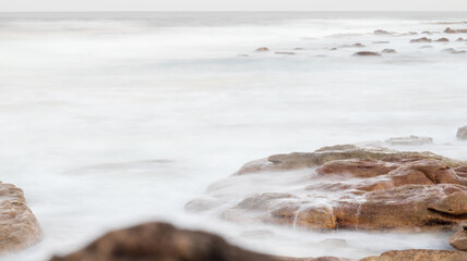Slow shutter speed photo of ocean water flowing over a rock, located at orange rocks in Margate South Africa