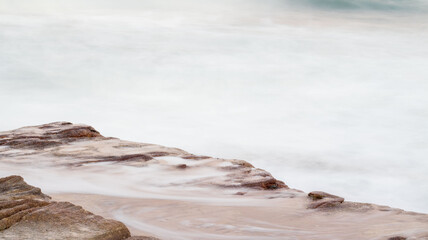 Slow shutter speed photo of ocean water flowing over a rock, located at orange rocks in Margate South Africa