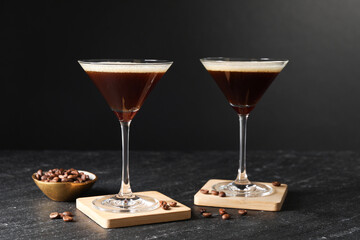 Glasses of delicious espresso martini and coffee beans on dark textured table
