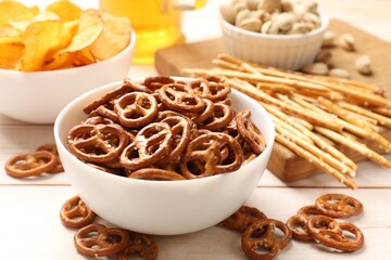 Delicious pretzel crackers and other snacks on white wooden table, closeup
