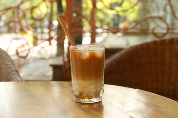 Glass of refreshing iced coffee and straw on wooden table outdoors
