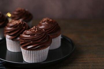 Tasty cupcakes with chocolate cream on wooden table, closeup. Space for text