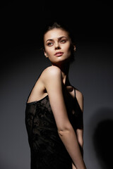 Naklejka premium Elegant woman in a black dress posing confidently against a dark background, showcasing beauty and grace with a soft smile.