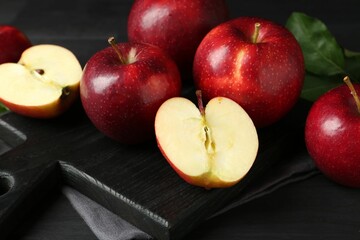 Whole and cut ripe red apples on black wooden table, closeup