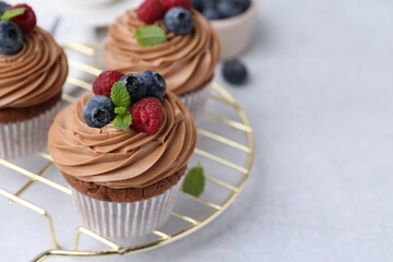 Tasty cupcakes with chocolate cream and berries on white table, closeup. Space for text