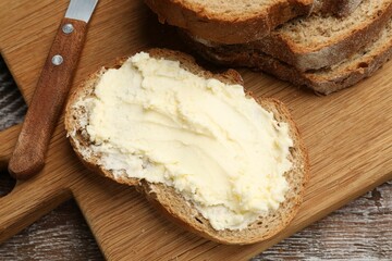 Fresh bread with butter and knife on wooden table, above view