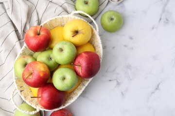 Different ripe apples in basket on white table, flat lay. Space for text
