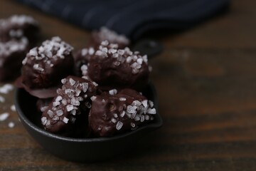Tasty chocolate candies with salt in bowl on wooden table, closeup. Space for text