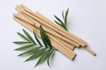 Bamboo drinking straws and palm leaves on white background, top view