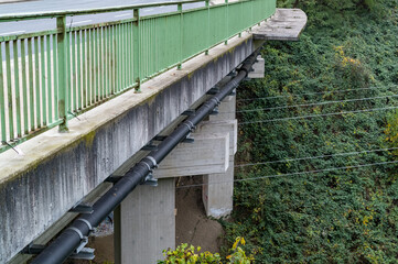 Large black pipes running under concrete bridge with green railing